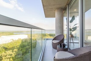 Ein Balkon mit Korbmöbeln, einer Glastrennwand und Blick auf ein Gewässer sowie Grünflächen.