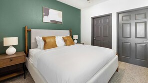 A hotel room with a bed, two bedside tables with lamps, a green wall, and a door. - Landing | Chic 2BD, Gym, Courtyard (Allen)