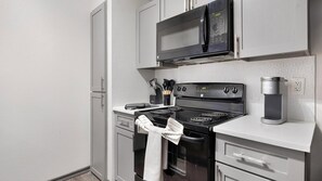 A compact kitchenette with a microwave, stove, and coffee maker. - Landing | Chic 2BD, Gym, Courtyard (Allen)