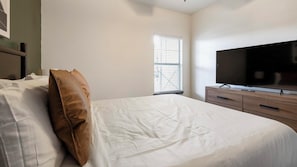 Una camera da letto con un letto, una televisione su una cassettiera in legno e una finestra con persiane.