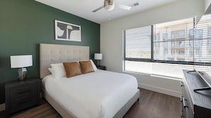 Ein modernes Schlafzimmer mit einem Bett, zwei Nachttischen, einem Deckenventilator und einem Fenster mit Jalousien.