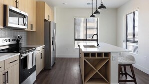 A modern kitchen with a built-in microwave, stainless steel appliances, and a large island with bar stools. - Landing | Incredible 2BD, Game Room, Gym (Goodyear)