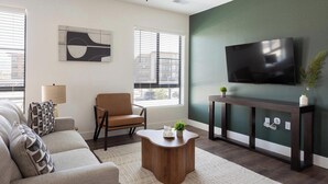 A modern living room with a sofa, armchair, coffee table, and a flat-screen TV mounted on a green wall. - Landing | Incredible 2BD, Game Room, Gym (Goodyear)