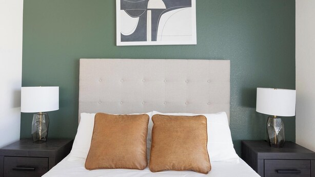 A hotel room with a bed, two nightstands, two lamps, and a wall art piece. - Landing | Incredible 2BD, Game Room, Gym (Goodyear)