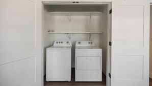 A laundry room with two white washing machines and a dryer, with shelves above for storage. - Landing | Incredible 2BD, Game Room, Gym (Goodyear)
