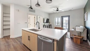 A modern kitchen with a dishwasher, a sink, and a dining area with a table and chairs. - Landing | Stylish 1BD, Gym, Courtyard (Goodyear)