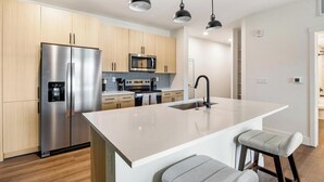 A modern kitchen with stainless steel appliances, a central island with seating, and a walk-in pantry. - Landing | Stylish 1BD, Gym, Courtyard (Goodyear)