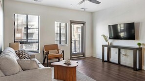 A modern living room with a sofa, armchair, coffee table, and a TV mounted on the wall. - Landing | Spectacular 1BD, Gym, Game Room (Goodyear)