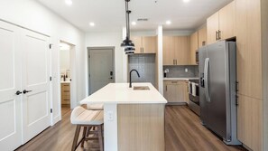 Een moderne keuken met een centraal eiland, roestvrijstalen apparatuur en licht houten kastjes.