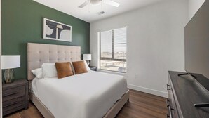 A bedroom with a large bed, two bedside lamps, a ceiling fan, a window with blinds, and a painting on the wall. - Landing | Incredible 2BD, Game Room, Clubhouse (Goodyear)
