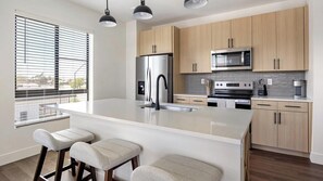 Une cuisine moderne dotée d’un îlot central, d’appareils électroménagers en acier inoxydable et d’armoires en bois.
