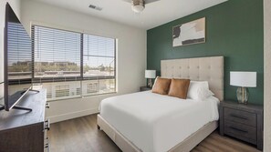 Une chambre d’hôtel avec un grand lit, deux tables de chevet avec des lampes, une vue dégagée grâce à de grandes fenêtres du sol au plafond et un mur d’accent de couleur verte.
