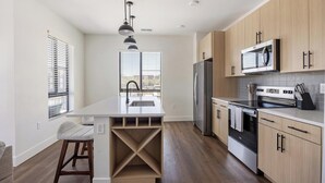 A modern kitchen with a central island, stainless steel appliances, and wooden cabinets. - Landing | Incredible 2BD, Game Room, Clubhouse (Goodyear)
