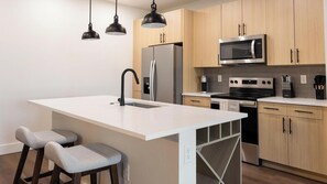 A modern kitchen with a central island, stainless steel appliances, and wooden cabinetry. - Landing | Beautiful 1BD, Clubhouse, Game Room (Goodyear)