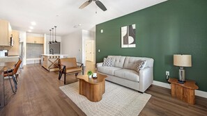 A modern living room with a sofa, coffee table, and a dining area with chairs and a table. - Landing | Stylish 1BD, Clubhouse, Game Room (Goodyear)