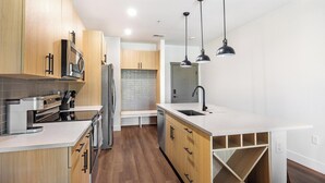 A modern kitchen with wooden cabinets, stainless steel appliances, and a white countertop. - Landing | Chic 1BD, Clubhouse, Game Room (Goodyear)