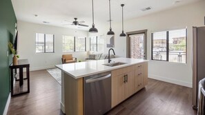 A modern kitchen with a central island, built-in appliances, pendant lighting, and large windows with blinds. - Landing | Stunning 2BD, Gym, Courtyard (Goodyear)