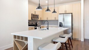 A modern kitchen with a central island, stainless steel appliances, and pendant lighting. - Landing | Beautiful 2BD, Game Room, Courtyard (Goodyear)