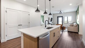 A modern kitchen with a central island, a built-in dishwasher, and pendant lighting. - Landing | Beautiful 2BD, Game Room, Courtyard (Goodyear)