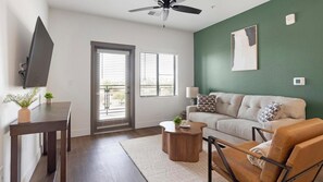 A living room with a flat-screen TV, a sofa, a coffee table, and a ceiling fan. - Landing | Beautiful 2BD, Game Room, Courtyard (Goodyear)