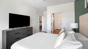 Ein Hotelzimmer mit einem großen Bett, einem flachbildfernseher, der an einer dunkelholzmöbel angebracht ist, und einer Nachttischlampe.