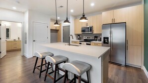 A modern kitchen with a central island, bar stools, stainless steel appliances, and pendant lighting. - Landing | Incredible 1BD, Clubhouse, Courtyard (Goodyear)