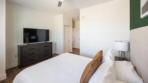 A hotel room with a bed, a television on a dresser, a lamp, and a door leading to another room. - Landing | Beautiful 1BD, Clubhouse, Courtyard (Goodyear)
