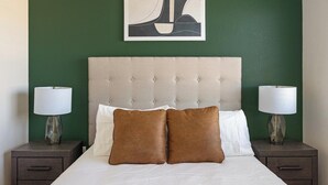 Ett hotellrum med en stoppad sänggavel, två sängbord med lampor och en säng med vita sängkläder och bruna kuddar.