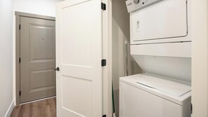 A laundry room with a front-loading washer and dryer, a closed door, and a wooden floor. - Landing | Stylish 1BD, Game Room, Courtyard (Goodyear)