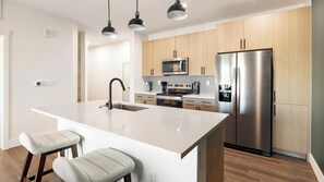 A modern kitchen with a central island, stainless steel appliances, and wooden cabinets. - Landing | Beautiful 1BD, Courtyard, Game Room (Goodyear)