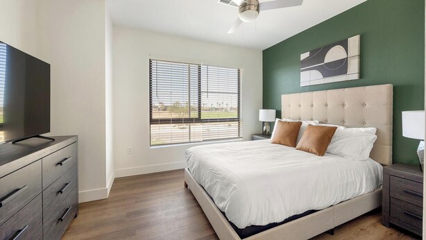 A bedroom with a bed, a television on a dresser, and a window with blinds. - Landing | Stunning 1BD, Game Room, Gym (Goodyear)