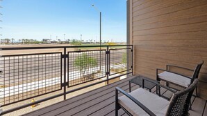 A balcony with a view of a parking lot and distant buildings, equipped with a metal railing and two chairs. - Landing | Stunning 1BD, Game Room, Gym (Goodyear)