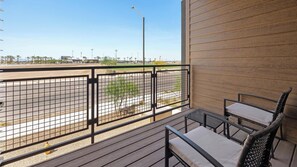 Ein Balkon mit Blick auf einen Parkplatz und entfernte Gebäude, ausgestattet mit einem Metallgeländer und zwei Stühlen.