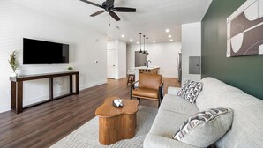 Een moderne woonkamer met een flatscreen televisie, een houten salontafel, een leren bank en een plafondventilator.