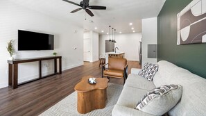 A modern living room with a flat-screen TV, a wooden coffee table, a leather sofa, and a ceiling fan. - Landing | Stunning 1BD, Courtyard, Clubhouse (Goodyear)