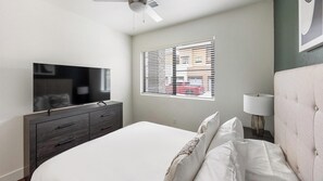 A bedroom with a bed, a TV on a dresser, a window with blinds, and a ceiling fan. - Landing | Modern 1BD, Clubhouse, Game Room (Goodyear)