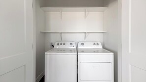 A laundry room with two white Whirlpool washers and dryers, a white ceiling, and a white door. - Landing | Incredible 2BD, Clubhouse, Gym (Goodyear)