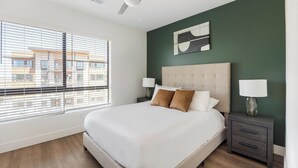 Ein modernes Schlafzimmer mit einem großen Bett, zwei Nachttischen mit Lampen, Blick durch raumhohe Fenster und einer grünen Akzentwand.
