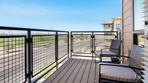 A balcony with a view of a sports field, a seating area with a table and chairs, and a building with a modern design. - Landing | Spectacular 2BD, Courtyard, Gym (Goodyear)