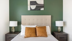 A bed with a tufted headboard, two bedside lamps, and a wall art piece above. - Landing | Spectacular 2BD, Courtyard, Gym (Goodyear)