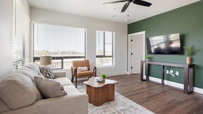 Ein Wohnzimmer mit Sofa, Sessel, Couchtisch und Fernseher an einer grünen Wand.
