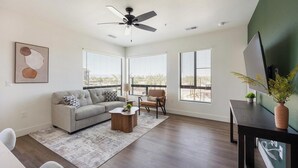A modern living room with a gray sofa, a coffee table, and a TV on a stand. - Landing | Stylish 2BD, Gym, Courtyard (Goodyear)