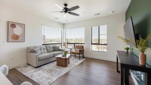A modern living room with a gray sofa, a coffee table, and a TV on a stand. - Landing | Stylish 2BD, Gym, Courtyard (Goodyear)