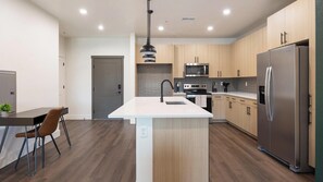 A modern kitchen with a central island, stainless steel appliances, and wooden cabinetry. - Landing | Incredible 1BD, Game Room, Gym (Goodyear)