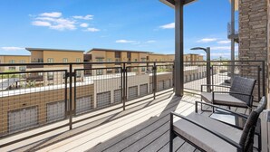 A balcony with a view of a parking lot and buildings, a metal railing, and a chair. - Landing | Stunning 1BD, Game Room, Gym (Goodyear)