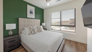 A bedroom with a bed, two bedside tables, a window with blinds, and a green wall. - Landing | Stunning 1BD, Game Room, Gym (Goodyear)