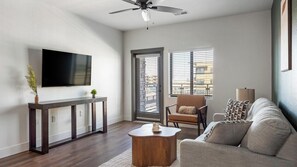 Una sala moderna con un televisor de pantalla plana, una consola de madera, un sillón de cuero y un sofá.