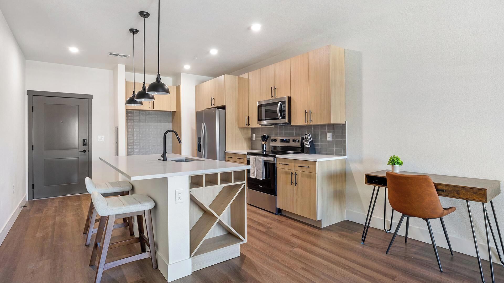 A modern kitchen with a central island, bar stools, a dining table with chairs, and a microwave.