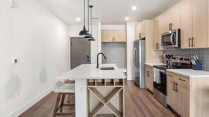 A modern kitchen with a central island, stainless steel appliances, and wooden cabinetry. - Landing | Stylish 2BD, Gym, Game Room (Goodyear)