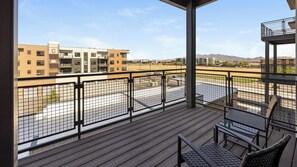A balcony with a view of a parking lot and buildings, featuring a wooden deck and metal railings. - Landing | Stylish 2BD, Gym, Game Room (Goodyear)